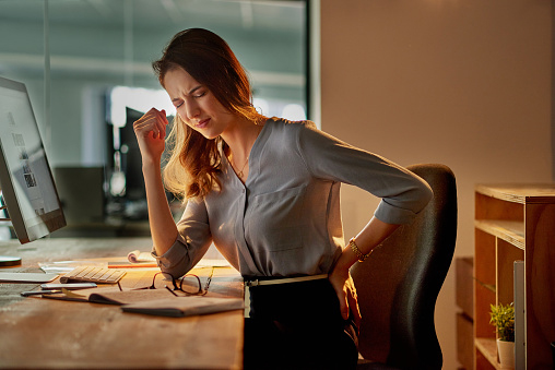 Woman sitting down and holding her breath and putting her back on her back while in the office working