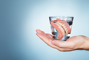 Cup of water contianing a set of dentures from at Singing River Dentistry in Athens, AL