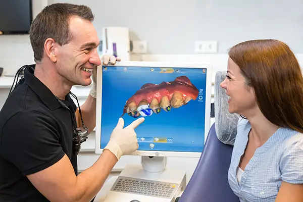 A dentist showing a patient a 3D CAD/CAM dental restoration model on a monitor during a consultation.