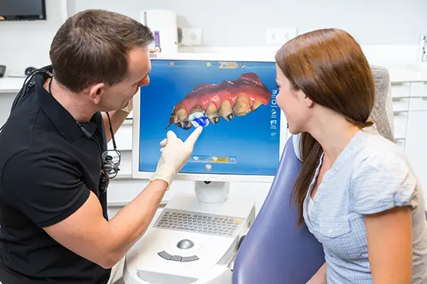 Dentist explaining a same-day crown procedure to a female patient using a digital 3D imaging screen in a modern dental office.