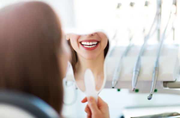 Woman looking at her smile in a mirror after getting restorative dental treatment at Singing River Dentistry