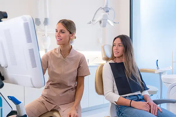 A dentist showing a female patient her dental X-ray results on a screen, discussing treatment options during an exam.