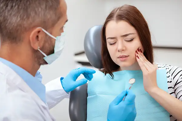 Female patient in a dental chair, holding her jaw and describing tooth pain to a dentist during an emergency appointment.