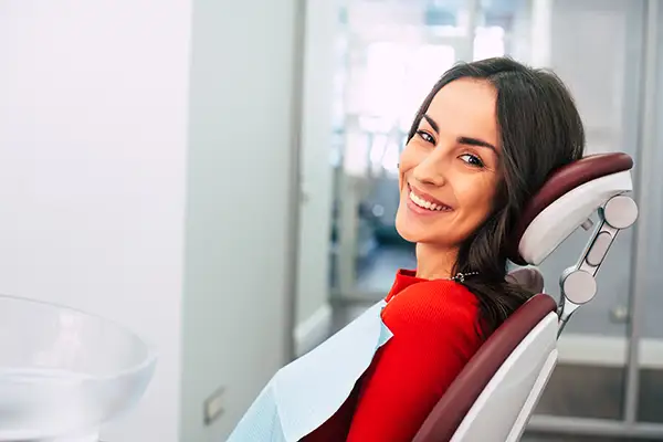 A woman smiling brightly in the dentist chair with a bib on, waiting for her first dental appointment.